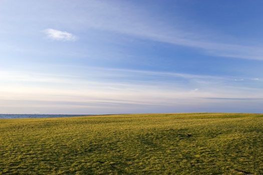 Green Field and blue sky near the sea at late afternoon light.