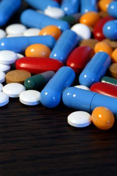 Collection of assorted pills on a dark wood table. Shallow depth-of-field.
