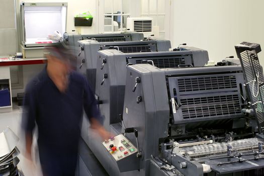 Motion blur on a printing company employee, as he runs a four colour printing press.  Shot with slow shutter speed with room lighting.

