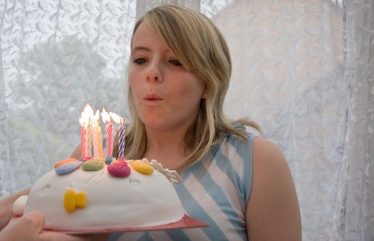 bpretty teenage girl blowing out the candles on her birthday cake.