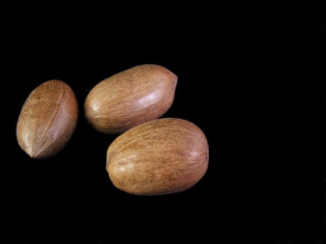 Three unshelled pecans against a black background.