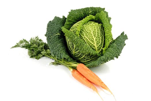 Single green cabbage with a bunch of raw crunchy orange carrots on a reflective white background