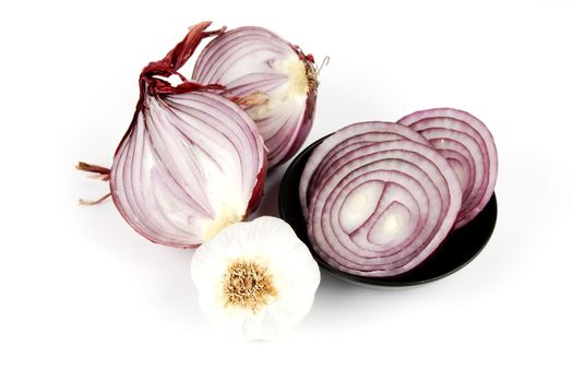 Raw red onion cut in half with slices in a dish and garlic on a reflective white background