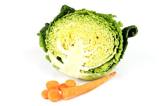 Half a raw green cabbage with a single chopped carrot on a reflective white background