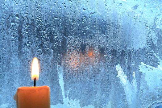 Candle with burning flame on background with frozen wet window