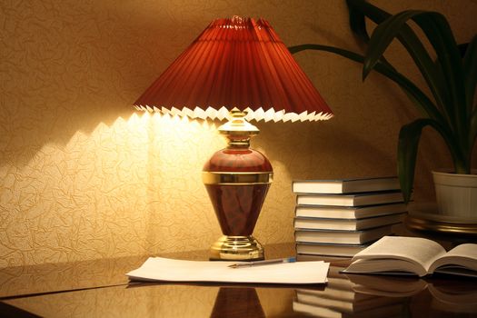 Evening home interior with luminous lamp and stack of books on the table