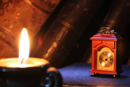 Vintage still life with old wooden clock, burning candle and books