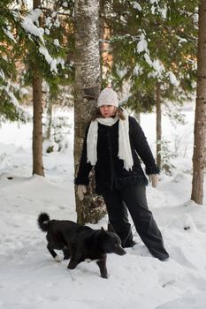 Happy middle-aged women with dog having fun on winters day in forest.