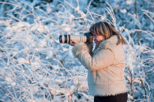 Happy middle-aged women photographer on winters day in forest.