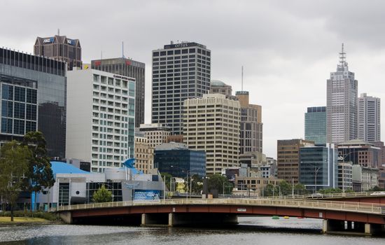 Melbourne city skyline against bridge over yarra river, cloudy skies