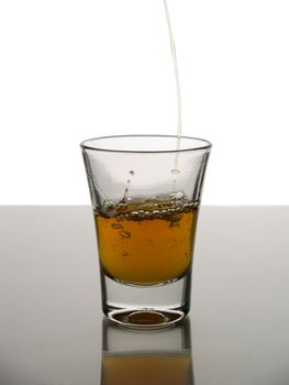 Pouring a shot of whisky on white background over gray floor.