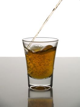 Pouring a shot of whisky on white background over gray floor.