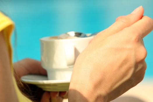 Woman drinking a cup cappuccino by the pool