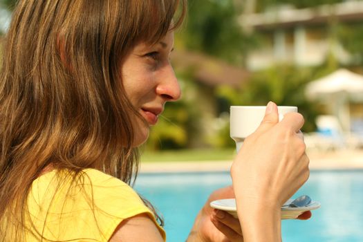 girl holding a cup coffee by the pool