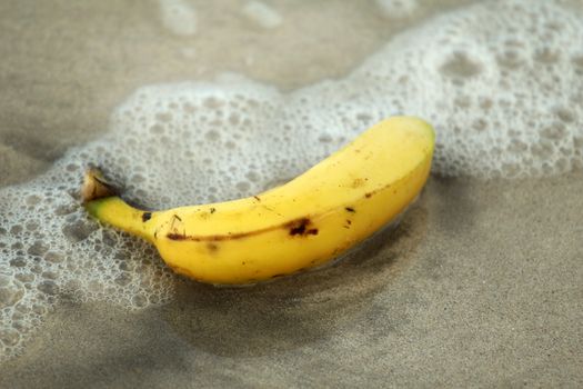 single banana lying in water on the beach