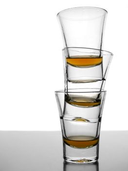 A pile of three almost empty shots of whisky on white background over gray floor.