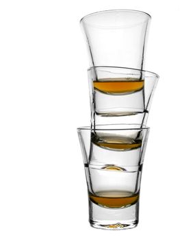 A pile of three almost empty shots of whisky on white background.