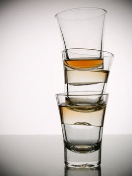 A pile of three almost empty shots of whisky on white background over gray floor.