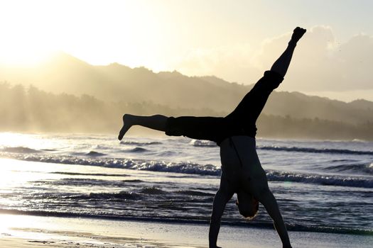 man turning cartwheel on the beach by sunset