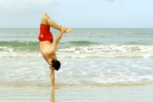 man handstanding on one hand on the caribbean beach