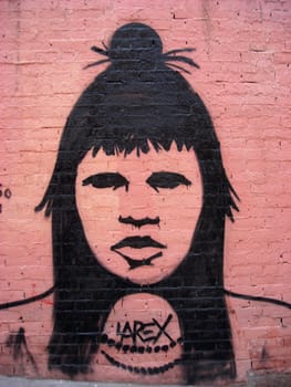 Graffiti of a tribal woman on a pink brick wall signed by the author