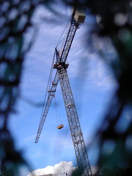 Tower crane watched from a hole in the fence of a work.