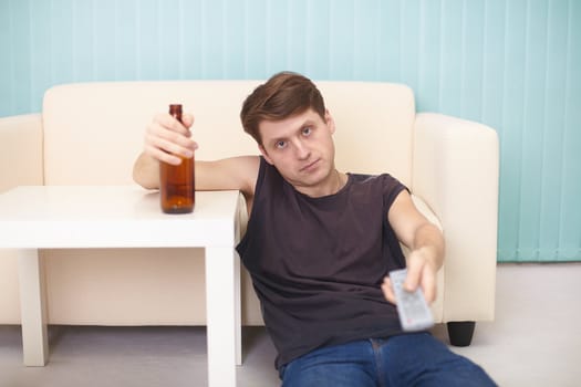 A drunk guy with a bottle of beer, the TV changes channels, sitting on the floor