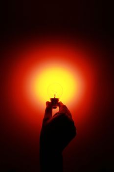 a hand holding a glowing red light bulb 
