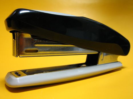 Metal stapler on a yellow background the left-side view