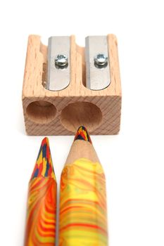 Two multi-coloured pencils before a wooden sharpener for pencils 