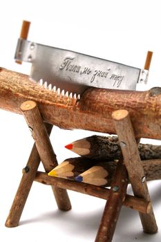 Three color pencils made of branches of a tree under a saw and a log