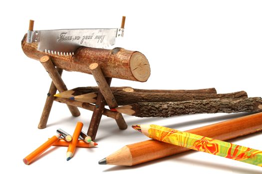 Pencils from natural wood of various type and the size near to a saw and a log