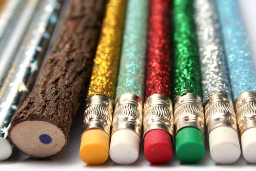 Unusual pencil made of natural wood among multi-coloured sparkling pencils