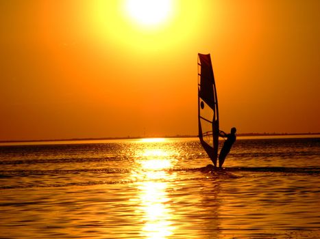 Silhouette of a windsurfer on waves of a gulf on a sunset