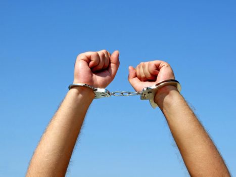 The hands of the men chained in handcuffs, on a background of the blue sky