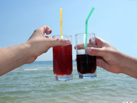 Two man's hands with glasses of cocktails on a background of the sea