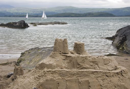 Sand castle on seas edge with two yachts sailing by.