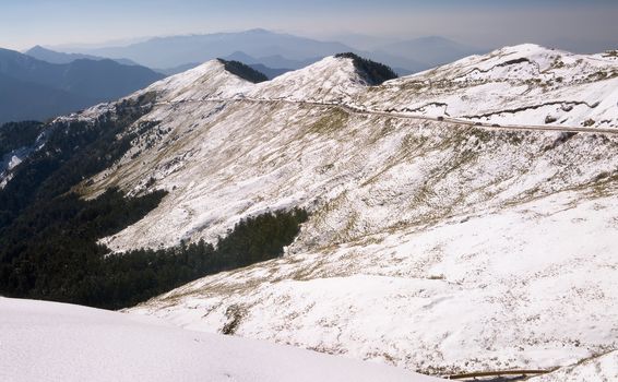 Snow white landscape with mountain transport road and forest.