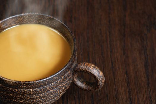 A macro, selective focus image of coffee with milk, in a wooden mug on a wood table.  Lots of copyspace available - Shallow depth of field with the focus on the handle.
