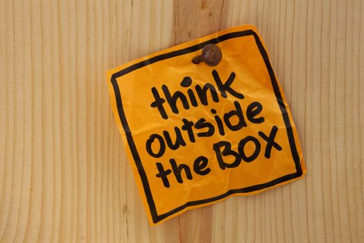 think outside the box - bright ornage reminder note nailed to a wooden wall