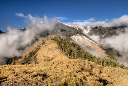 Dramatic landscape of mountain with white beautiful clouds and yellow grassland against blue sky.