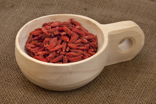 dried Tibetan goji berries (wolfberries) on a rustic unfinished wooden scoop, burlap background