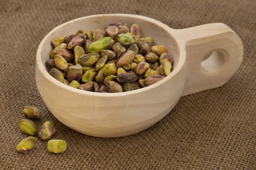 raw shelled pistachio nuts on a rustic, wooden scoop with brown burlap background