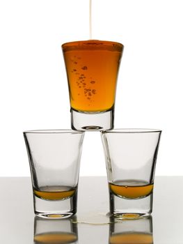 A shot being poured over two almost empty shots.