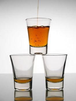 A shot being poured over other two almost empty shots.