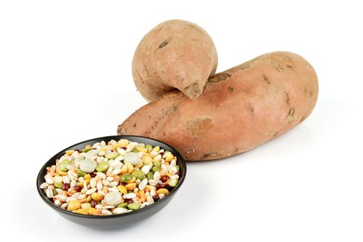Two raw unpeeled sweet potatoes with a small black dish of soup pulses on a reflective white background