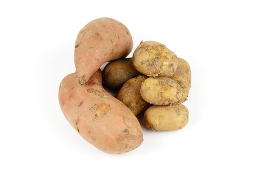 Small pile of brown unpeeled potatoes with two sweet potato on a reflective white background