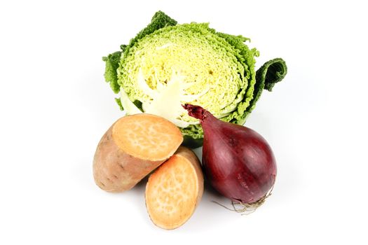 Half a raw green cabbage with a sweet potato cut in half and a single red onion on a reflective white background