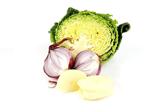 Half a raw green cabbage with a red onion cut in half and peeled potato slices on a reflective white background