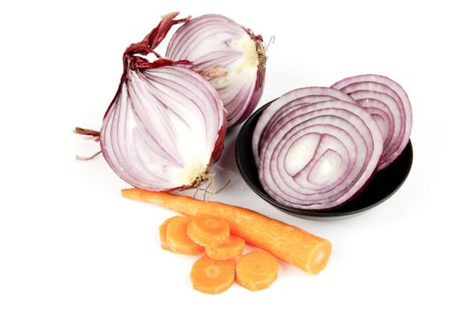 Raw red onion cut in half with slices in a dish and carrot on a reflective white background